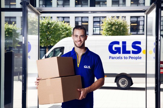 GLS driver with package in front of his vehicle in an office area