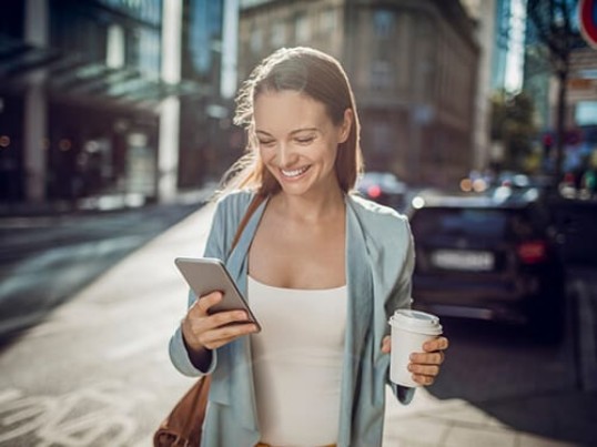 Junge Frau auf der Straße mit Handy und Coffee-to-go