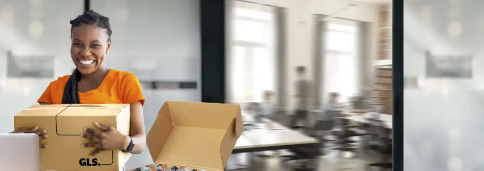 A smiling woman holding a GLS parcel in an office setting.