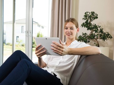 woman sitting on a couch and looking into a tablet