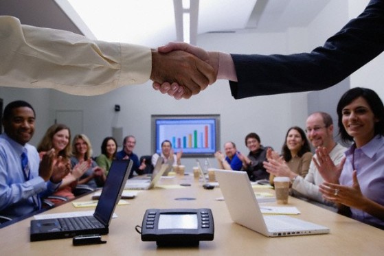 group of people in a conference room and two people in front shaking hands