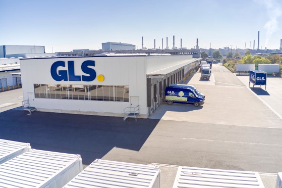 GLS terminaali aurinkoisena päivänä ja GLS:n sininen jakeluauto on terminaalin lastausalueella.