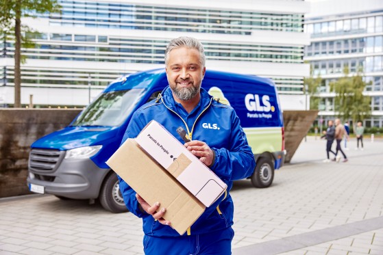 GLS-kuljettaja pitää käsissään kahta GLS-pakettia taustalla GLS-sähköinen jakeluauto