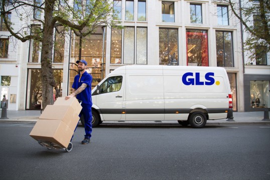 GLS delivery driver with parcels and a delivery van on a city street.