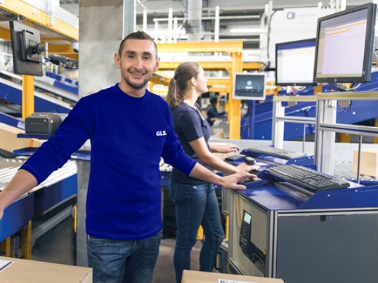 GLS France smiling employees sort parcels on a conveyor belt