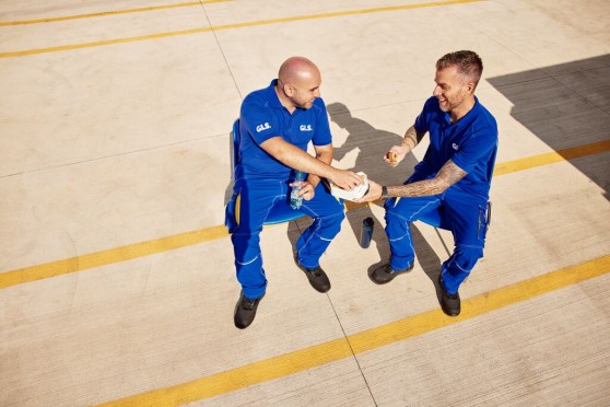 Two GLS employees taking a break at a logistics site, interacting in an outdoor work environment, illustrating initiatives related to quality of working life and workplace well-being (QLWC).