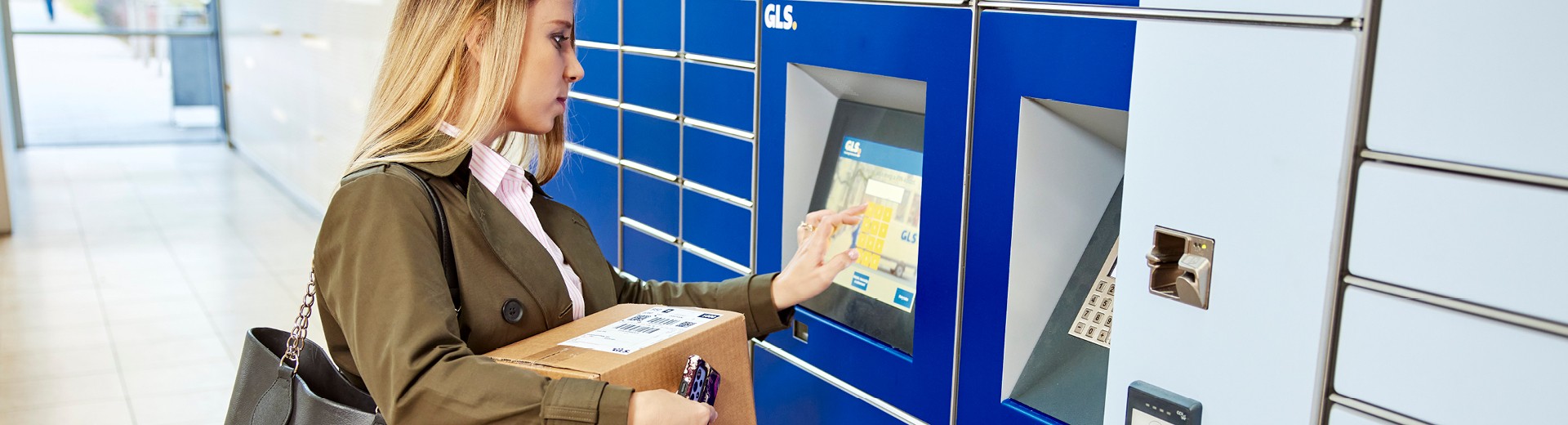 Femme récupérant un colis dans un casier automatique GLS, utilisant l’écran tactile pour entrer ses informations.