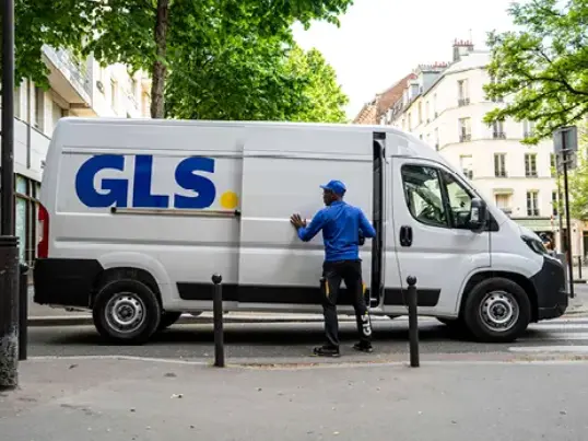 GLS driver standing next to a white GLS delivery van parked on a city street.