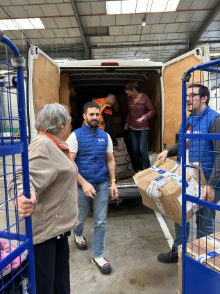 Volunteers and staff unload boxes from a van inside a warehouse, as part of a logistical solidarity operation.