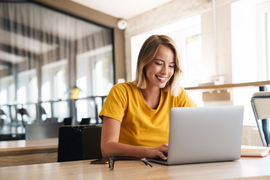 Smiling woman working on her laptop, managing her YourGLS account in a modern office