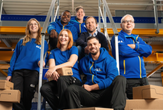 GLS delivery worker in a blue uniform using a handheld delivery terminal while holding a package.
