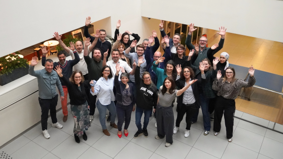 Group of smiling, diverse GLS employees waving at the camera in a modern office atrium.