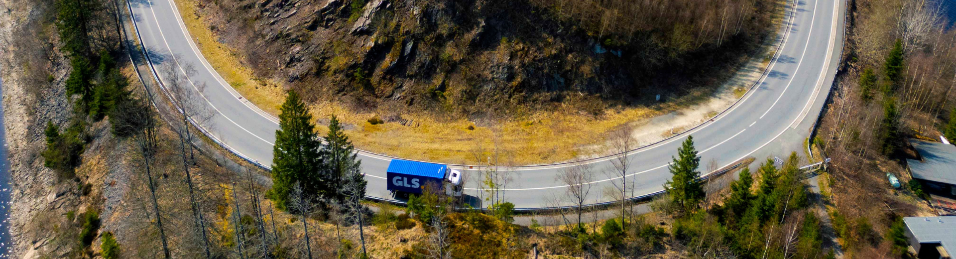 Blue GLS semi-trailer truck on a winding mountain road through a forested landscape.