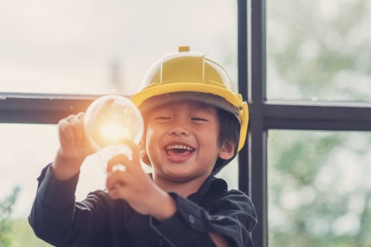 kid wearing a hard hat looking at a light bulb
