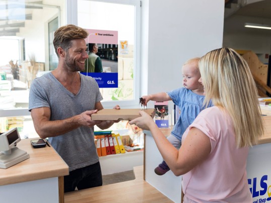 A woman with a phone in one hand and a parcel in the other entering a Parcel Shop