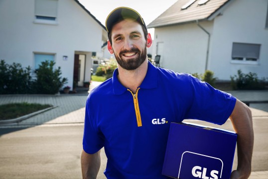 GLS kuriér stojaci s balíkom pred domom