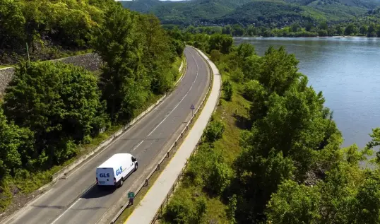 Delivery van driving along a mountain road beside a lake.
